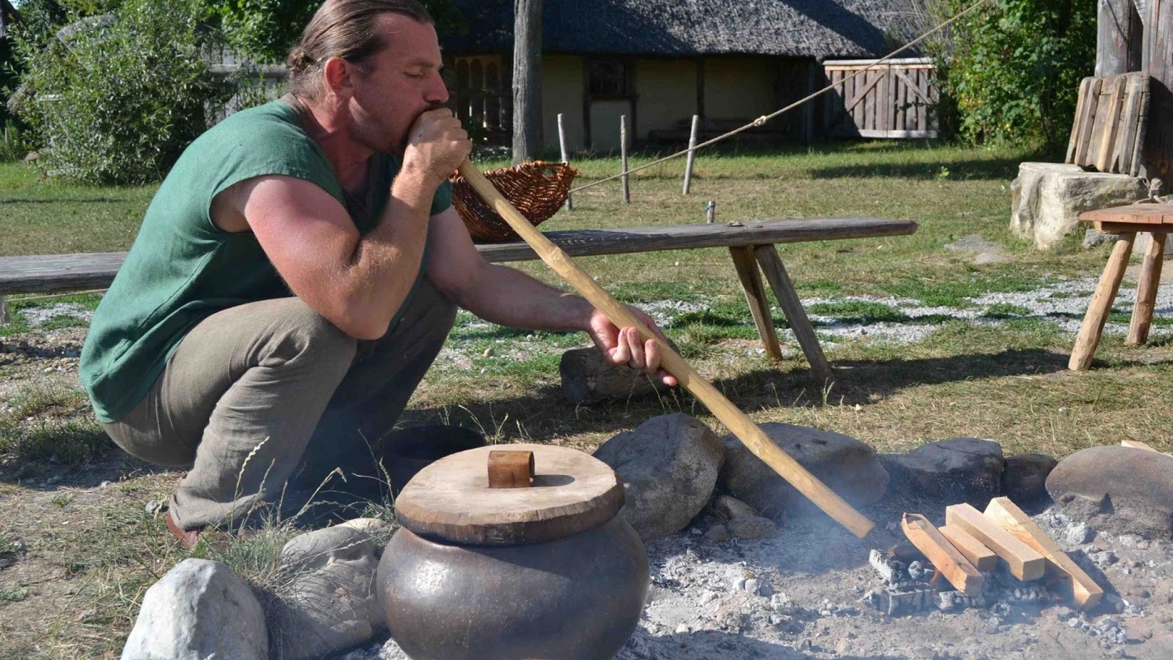 Bick auf einen Mann, der am Boden hockt und durch ein Feuerblasrohr bläst.