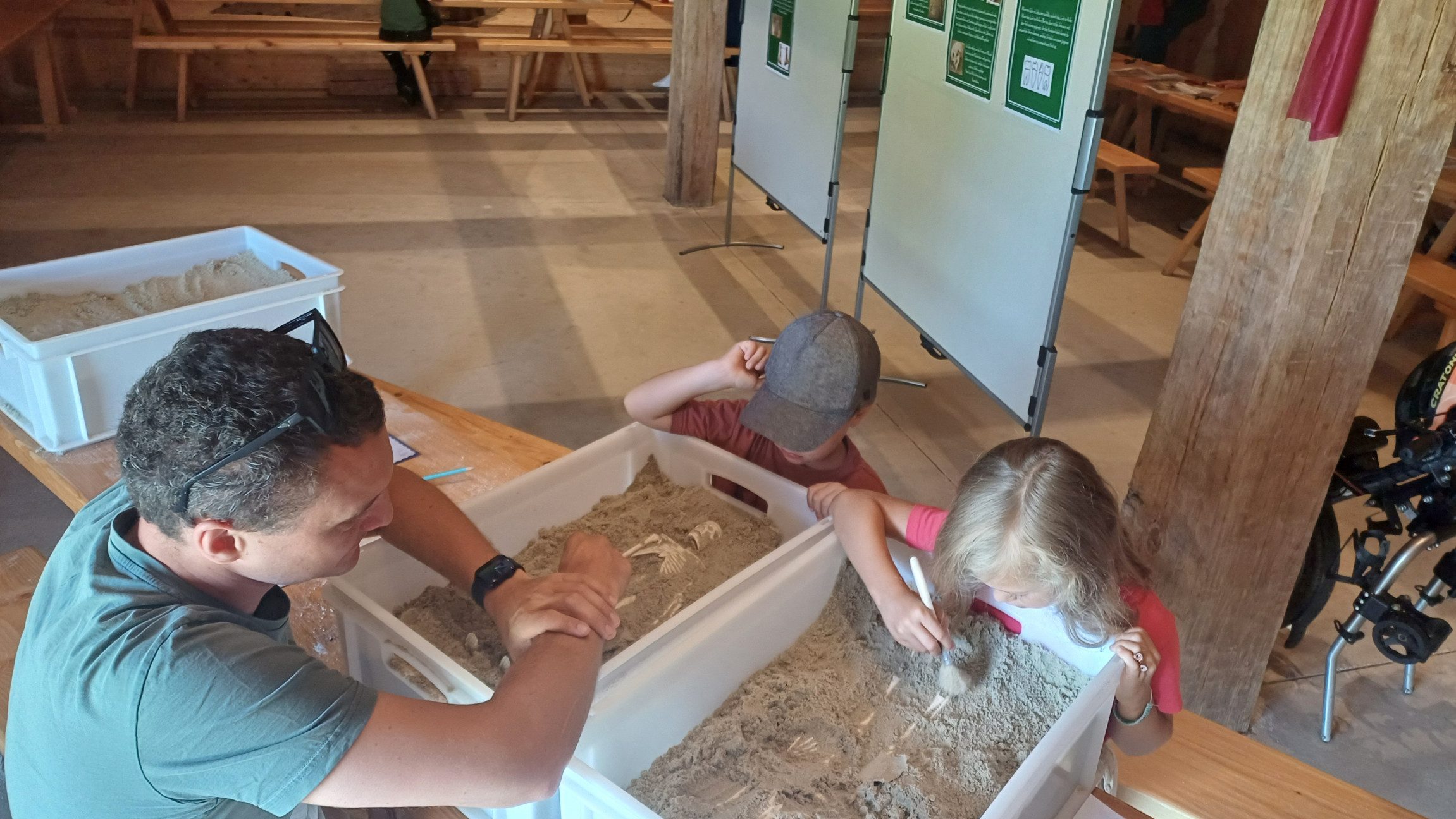 Zwei Kinder und ein Erwachsener, die über Plastikboxen mit Sitzen und etwas ausgraben.