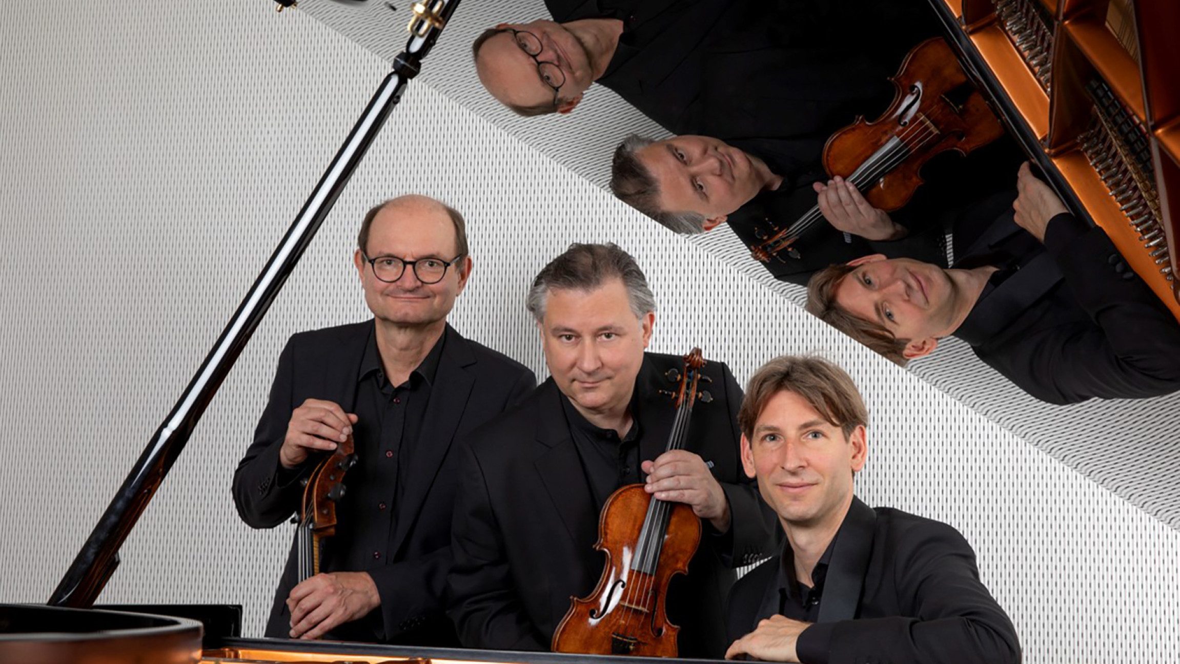 Gruppenfoto vom Amadeus Trio durch ein Klavier hindurch.