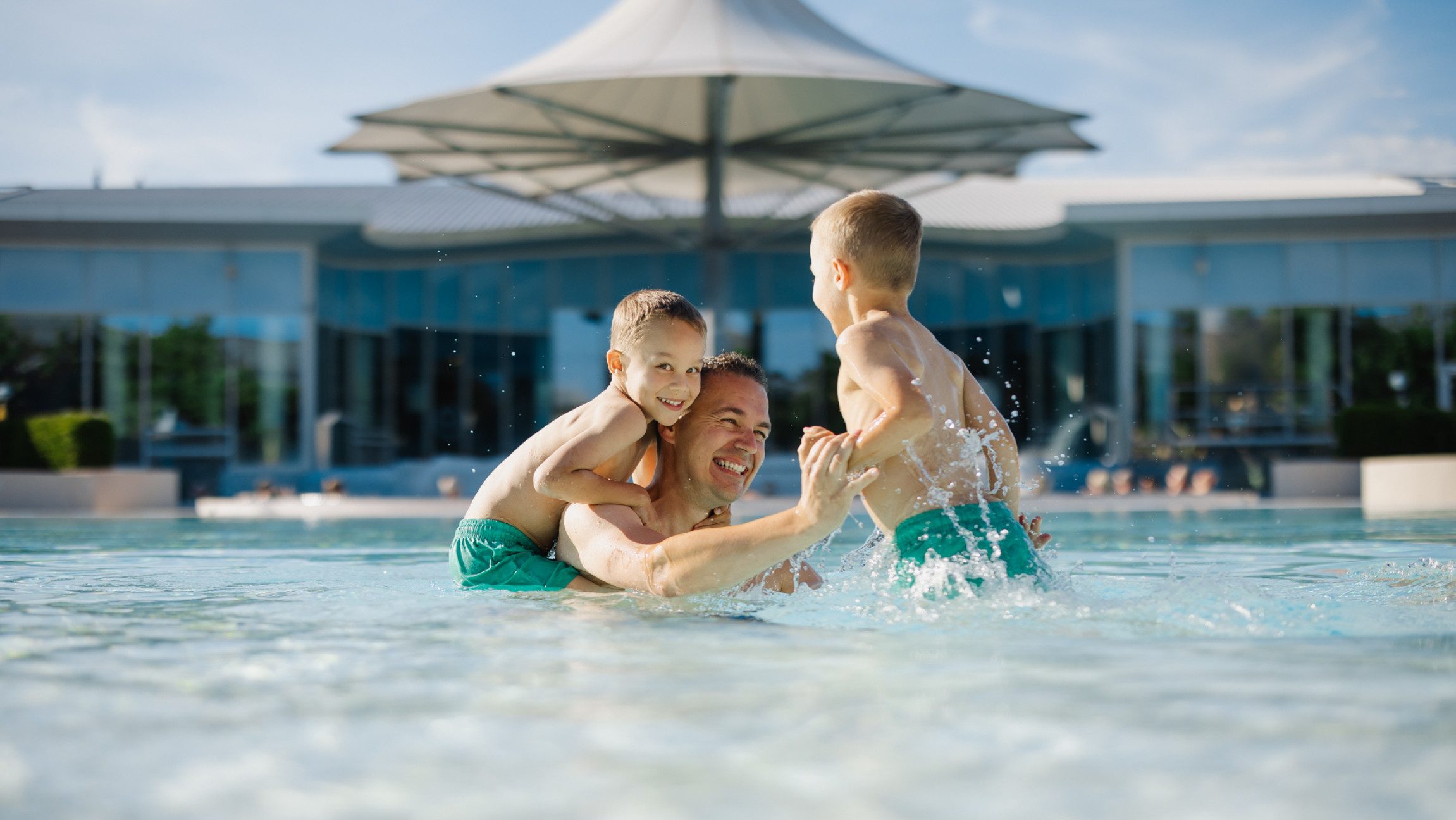 Blick auf einen Mann der mit zwei Kindern im Wasser spielt.