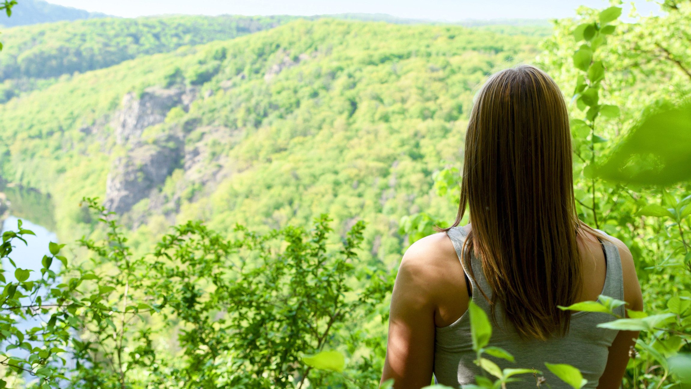 Blick auf eine Dame die im Wald sitzt und einer Erhöhung hinuntersieht.